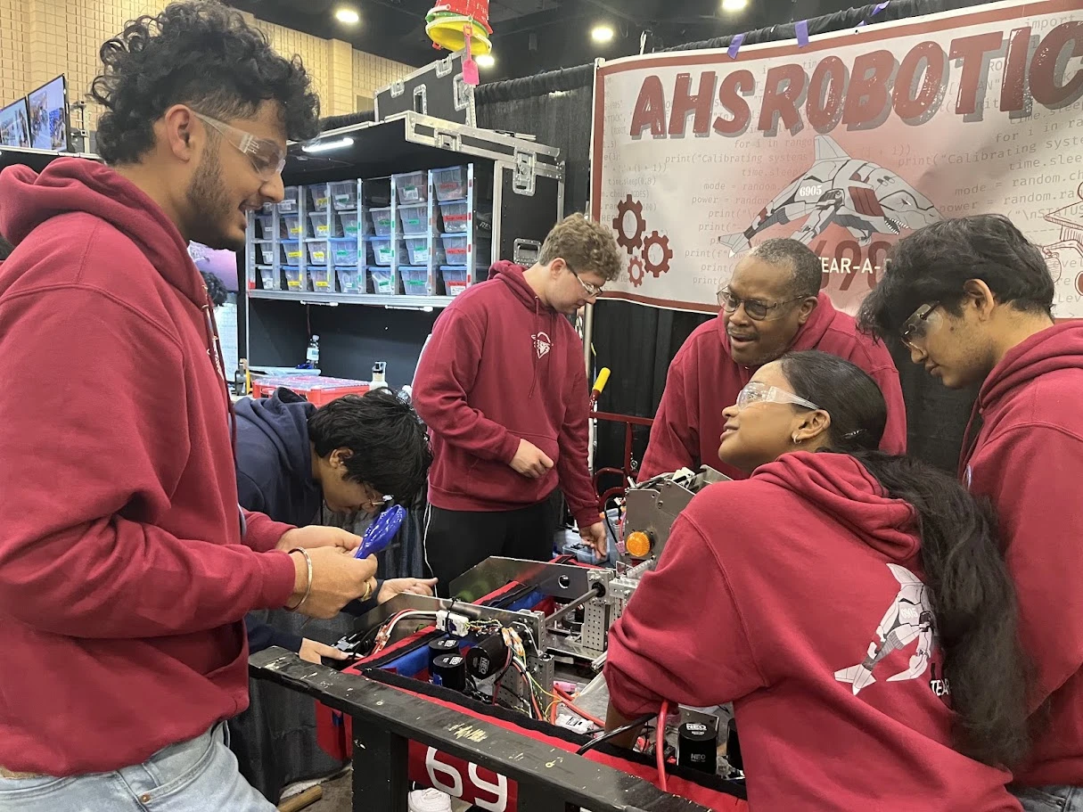 Students in A.R.C. hoodies working on the robot in the pit under the AHS Robotics banner