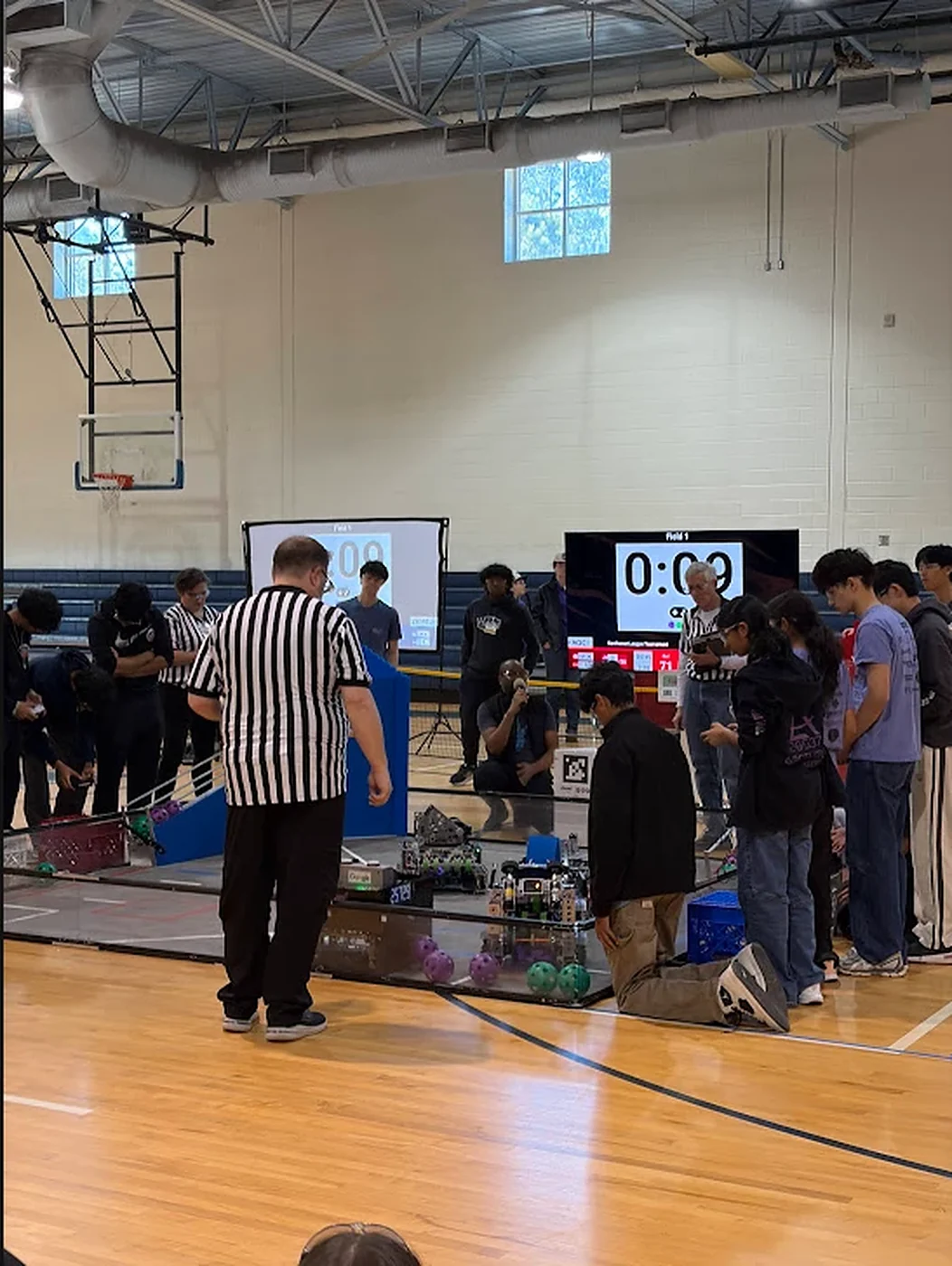 FTC match in progress in the school gym, with the scoreboard and referee
