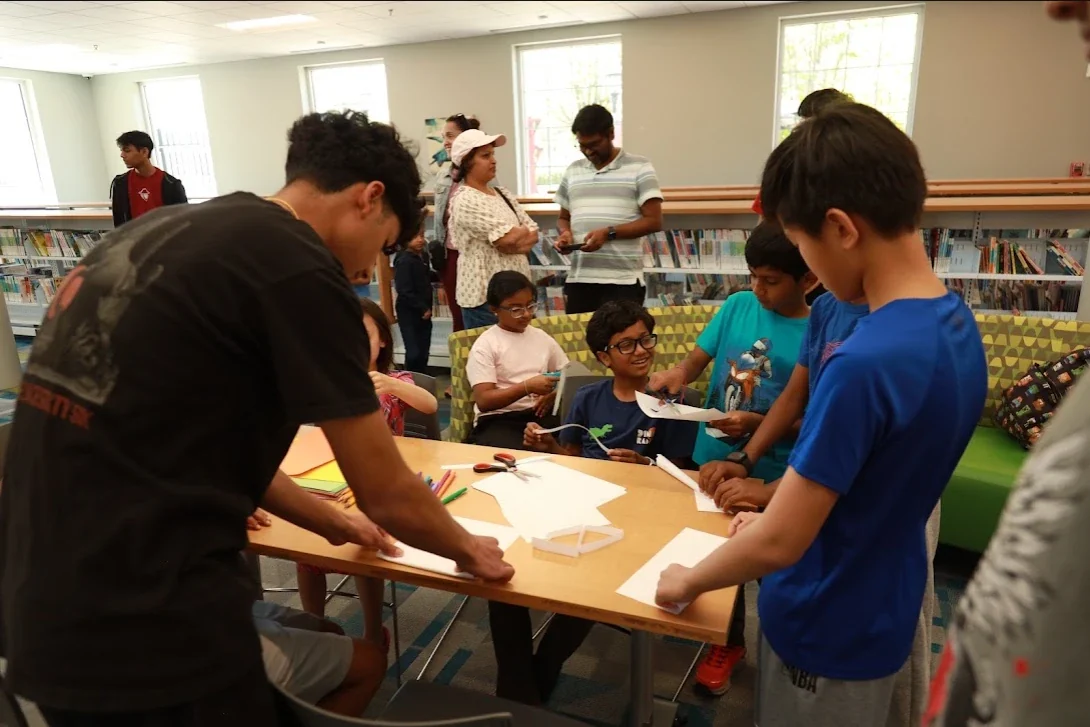 Club members leading a paper-craft activity for kids at a library outreach event