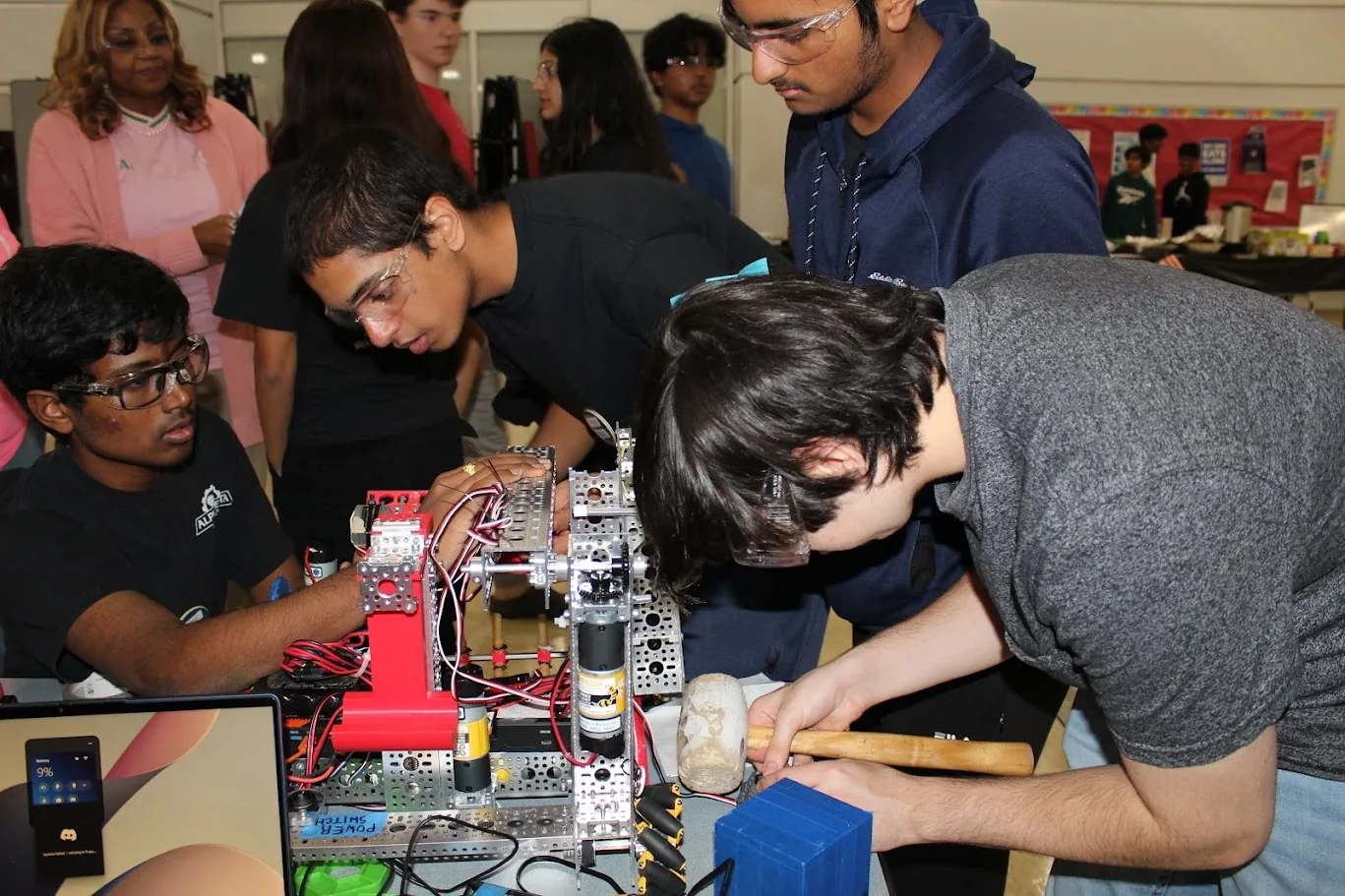 Students building and testing a robot together with a mallet and a laptop at an outreach event